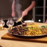 Ett fat Biff Rydberg står i förgrunden. I bakgrunden står en man och steker